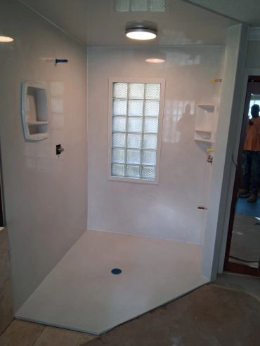 Newly installed white corner shower with built-in shelves and glass block window.