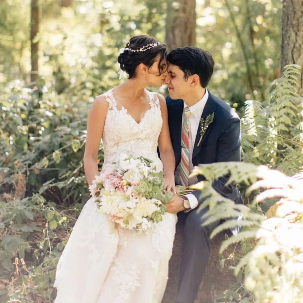 Bride and groom share a tender moment in a sunlit forest.