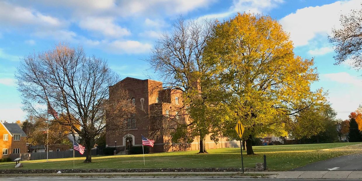 Autumn scene with flags, trees, and a brick building under blue sky.