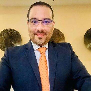 Man in a suit with an orange tie smiling at the camera.