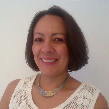 Smiling woman with short dark hair wearing a white crocheted top and a silver necklace.