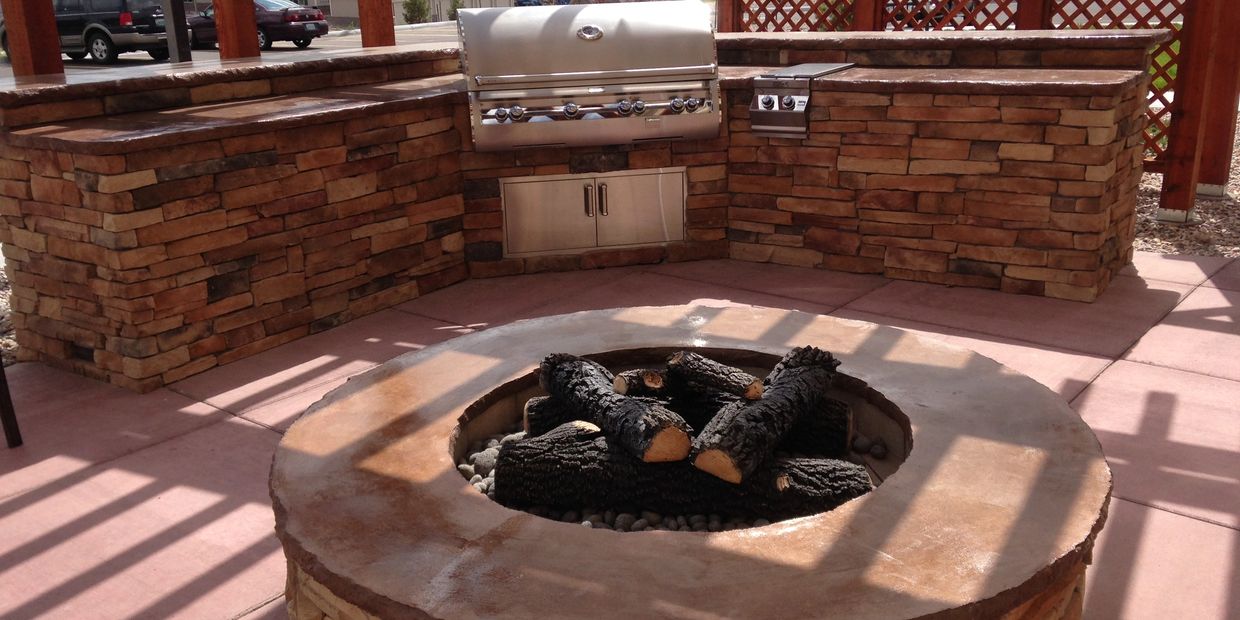 Outdoor kitchen with stone countertops and a fire pit with logs.