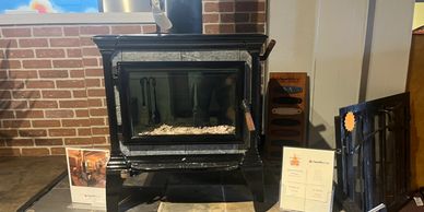 Black wood-burning stove displayed indoors with informational signs around it.