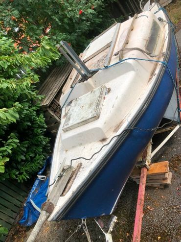 An old blue and white boat on a stand in a yard.