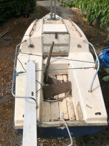 An old, weathered sailboat on land surrounded by greenery.