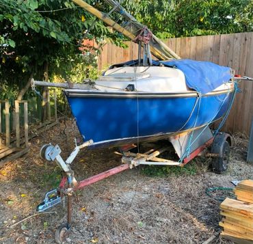 Small blue sailboat on a trailer in a backyard.