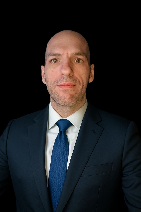 Professional man in a suit and blue tie against a black background.