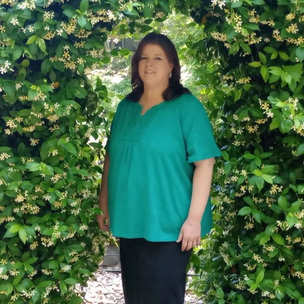 Woman standing in a floral archway of green leaves and small white flowers.