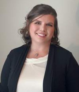 Professional headshot of a woman smiling warmly at the camera, wearing business-casual attire agains