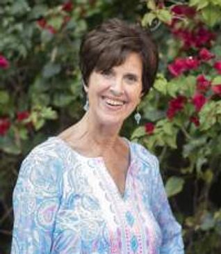 Professional headshot of a woman smiling warmly at the camera, wearing business-casual attire agains