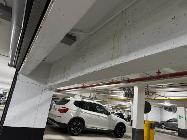 White SUV parked in indoor parking garage with concrete pillars.
