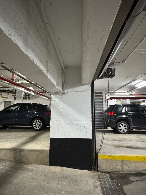 Concrete pillar painted white and black in a parking garage with parked cars.