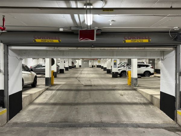 View of an underground parking garage with parked cars and concrete pillars.