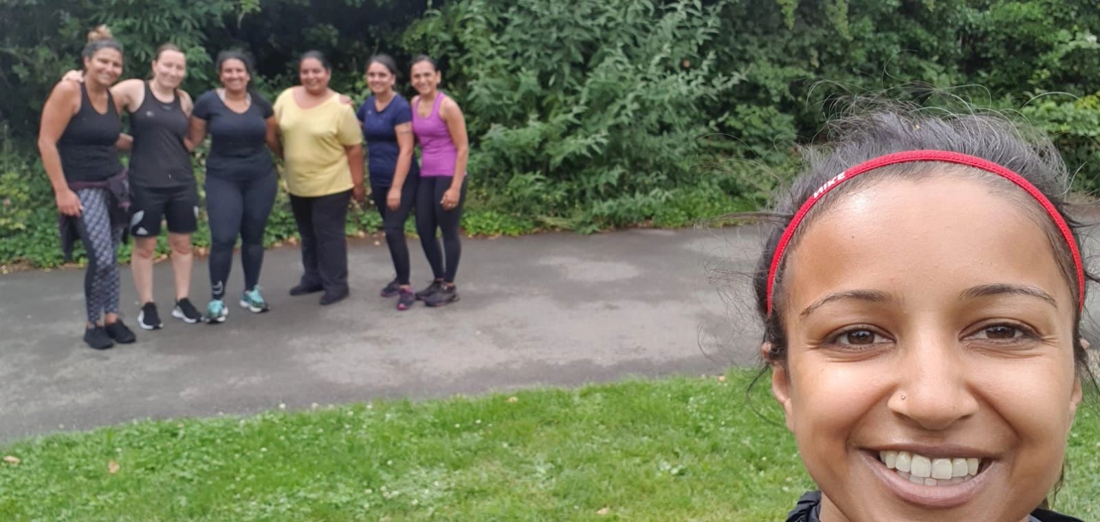 A group of seven women smiling outdoors, one taking a selfie.