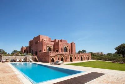 Large red brick mansion with a swimming pool under a clear blue sky.