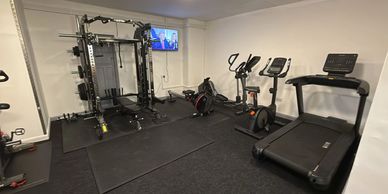 A home gym with various exercise machines and a TV on the wall.