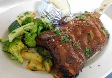 ribs, vegetables, and a baked potato on a plate