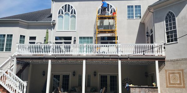 Worker standing on a scaffold cleaning windows on a large house.