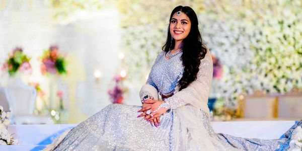 A smiling woman in an elegant silver traditional dress sitting gracefully.