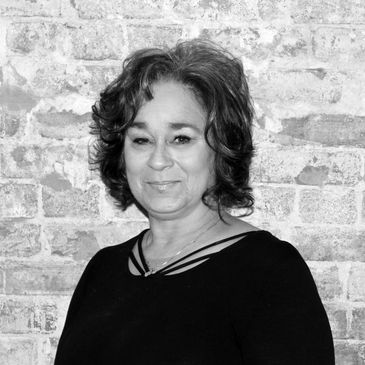Black and white portrait of a smiling woman against a brick wall.