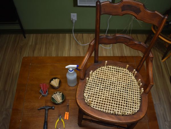 Wooden chair with cane seat being repaired on a table with tools.
