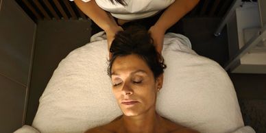 A woman receiving a relaxing head massage while lying on a spa bed.