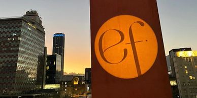 Sunset cityscape with 'ef' logo illuminated on a building wall.
