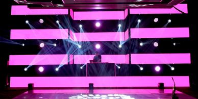 Escenario con luces moradas y DJ en cabina.