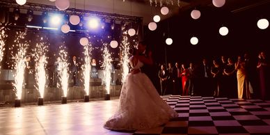 Pareja bailando bajo luces y chispas en una boda.