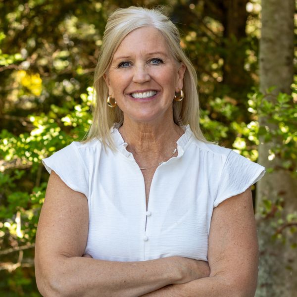 Smiling woman in white blouse stands outdoors with arms crossed.