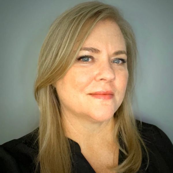 Portrait of a confident blonde woman with blue eyes and a slight smile.