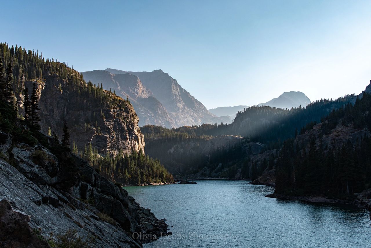 scenic mountain photo by Olivia Jacobs of the sunsetting on a large rock face and lake in Montana