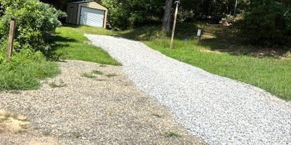 Gravel driveway leading to a small garage surrounded by trees.