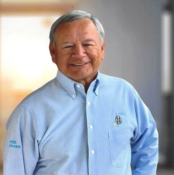 Smiling elderly man in light blue button-up shirt.