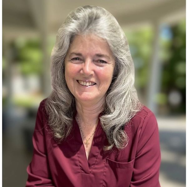 Smiling woman with gray hair in a maroon shirt.