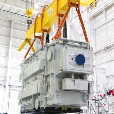 Large industrial transformer being lifted by crane in a factory.