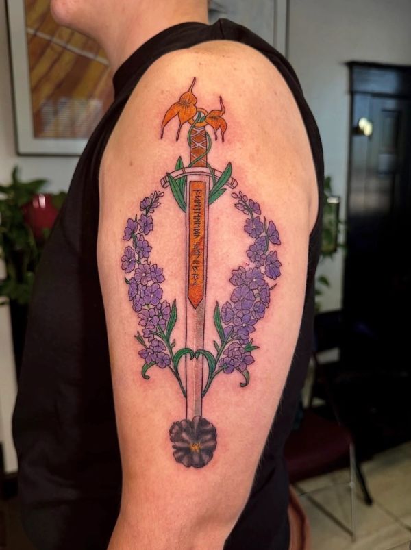 Sword tattoo with purple flowers on upper arm.