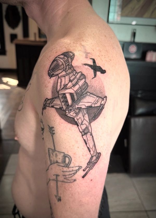 Tattoo of a spaceship and flying figure on upper arm.