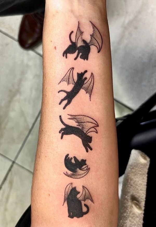 Tattoo of cats with bat wings on a forearm.