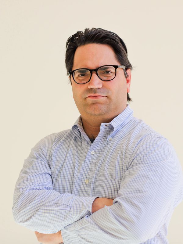 Confident man with glasses and crossed arms in a light checkered shirt.