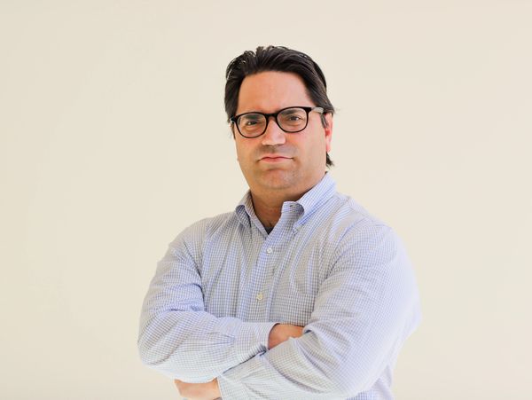 Confident man with glasses and crossed arms in a light checkered shirt.