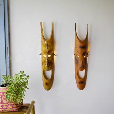 Two elongated wooden masks hanging on a white wall.
