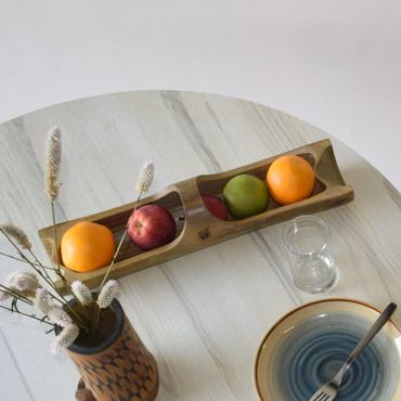 Wooden tray with fruits on a round table beside a vase and plate.