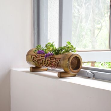Decorative bamboo planter with green plants and purple flowers on a windowsill.