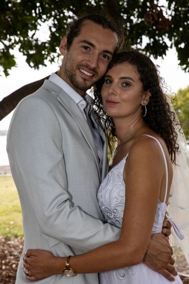 Newlywed couple embracing outdoors under a tree.
