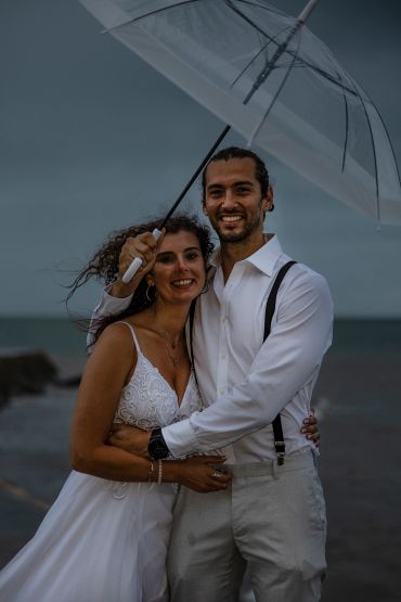 Couple embracing under a clear umbrella by the sea at dusk.