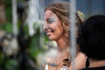 Portrait of a smiling woman with braided hair and a flower accessory, seen through a translucent surface.