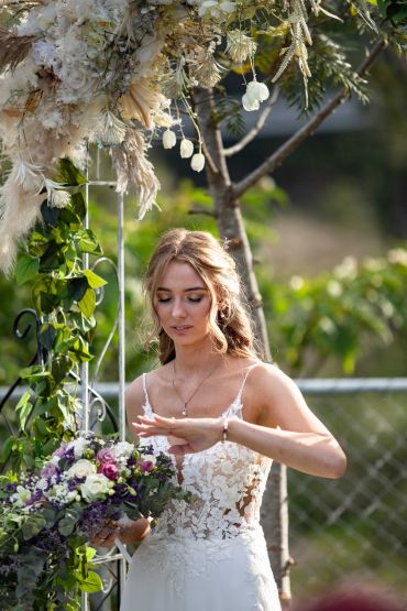 Bride in a lace wedding dress checking her ring during outdoor ceremony.