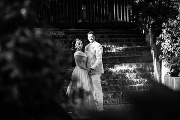 Bride and groom holding hands, smiling on stone steps in black and white.