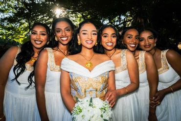 Bride with bridesmaids in white dresses smiling outdoors.